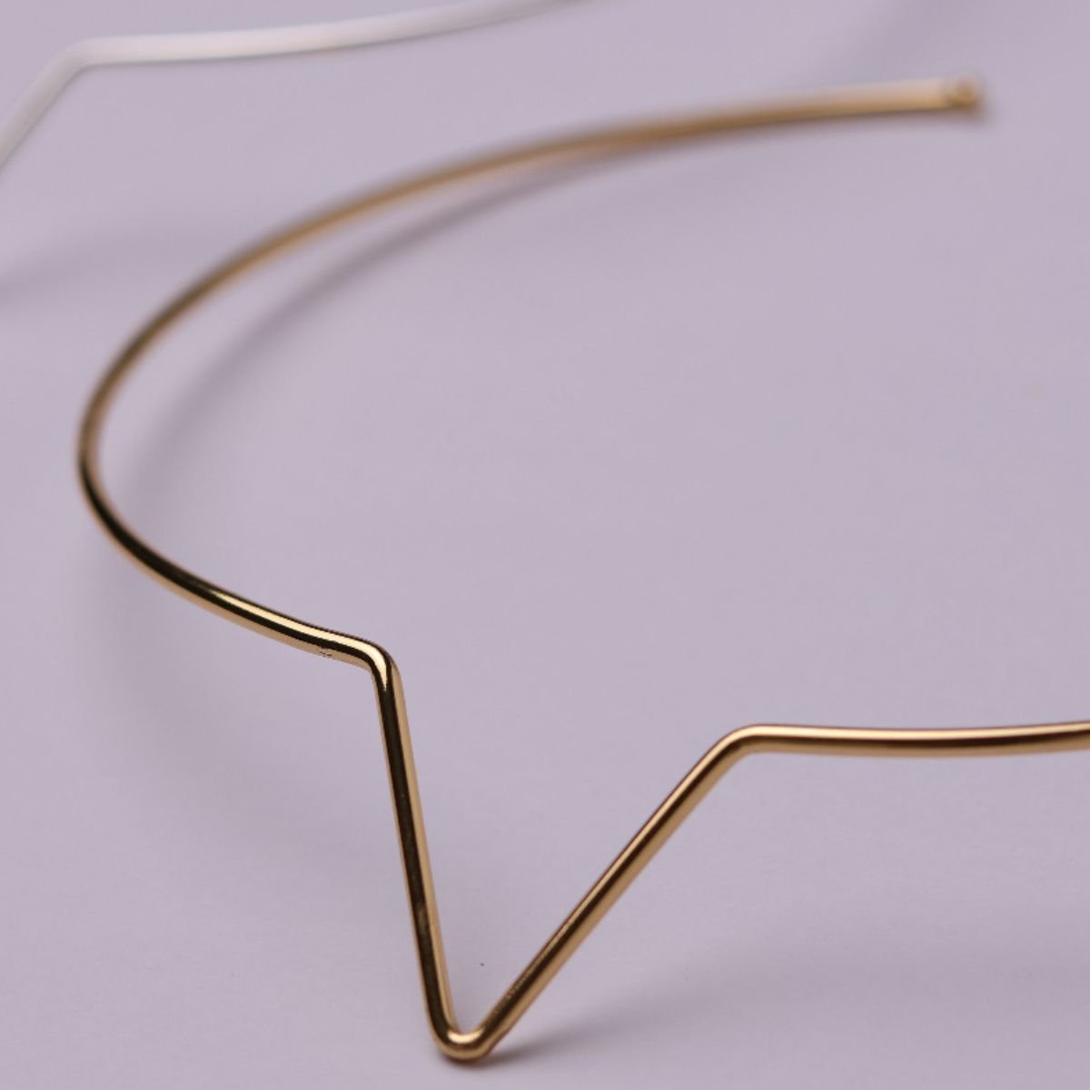 Choker dourada de aro rígido com desenho geométrico em V, produto da Permitta